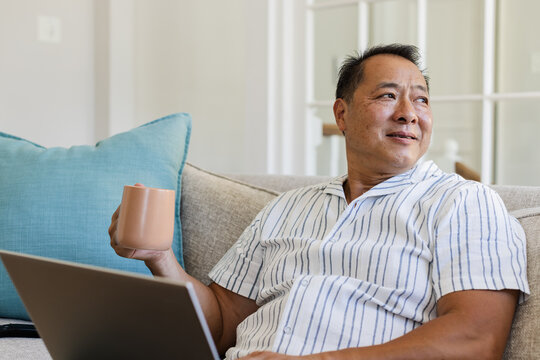 Senior man relaxing on sofa with coffee and laptop, enjoying leisure time