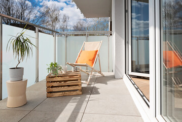 Modern home interior with a balcony with tiled floor, sun lounger and wooden coffee table. Window with glass and blue sky.  New apartment.