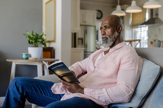 Senior man relaxing at home, reading book on comfortable sofa, enjoying leisure time