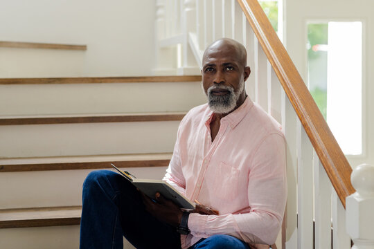 Senior man sitting on stairs reading book, enjoying quiet moment at home