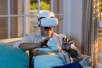 Senior man using VR headset on couch, experiencing virtual reality at home