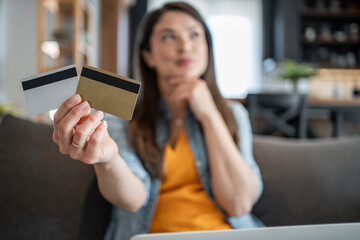 Woman choosing between two credit cards while online shopping at home