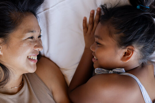 Mother and daughter lying on bed, sharing smiles and enjoying quality time