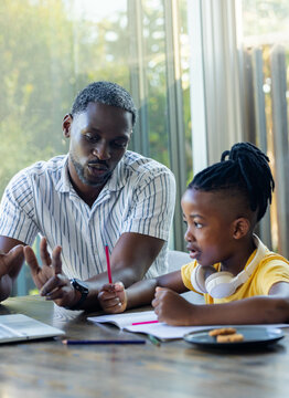 African American father helping son with homework at home, using laptop and notebook