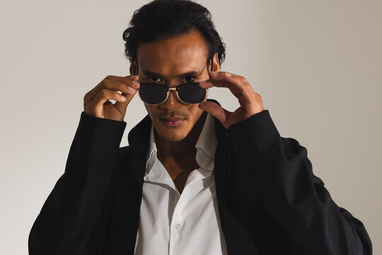 Confident man adjusting sunglasses wearing stylish black coat in fashion studio