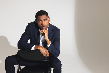 Confident man in suit sitting on chair, thoughtfully looking away in studio