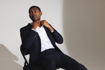Confident man in suit adjusting collar while sitting on chair in studio