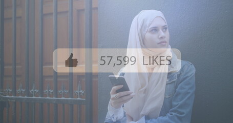Image of digital interface thumbs up with growing numbers on white speech bubble over woman in hijab