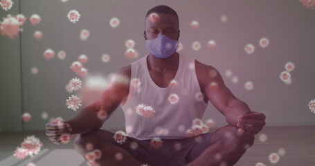 Covid-19 cells floating against african american man wearing face mask practicing yoga