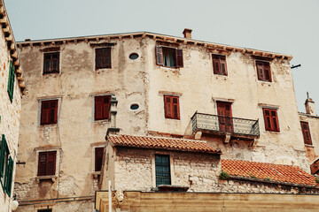 Rustic Mediterranean-style stone building with red shutters and tiled roof under clear sky