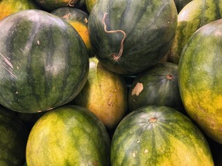 A close-up shot of a pile of fresh watermelons at a market. The image highlights their striped rinds and green and yellow hues