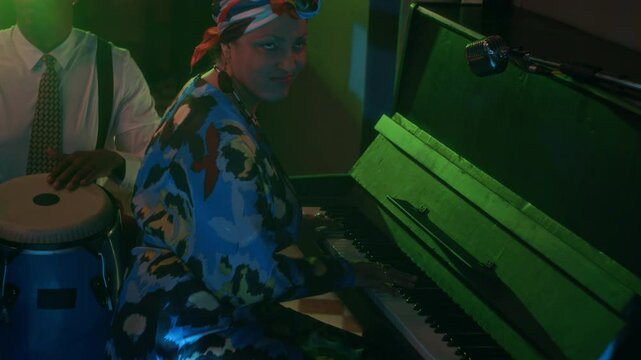 Jazz trio performing under neon lights. Saxophonist in foreground, percussionist with congas at center, and female pianist in colorful attire creating vibrant, rhythmic scene in neon bar