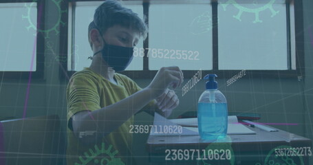 Image of covid 19 icons and numbers changing over schoolboy in face mask using hand sanitizer