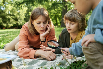 Portrait of happy family lying on picnic blanket in park together and using magnifying glass...