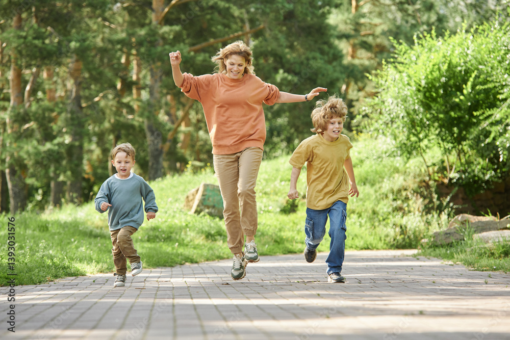 Wall mural full length front view of cheerful mother with two boys running playfully towards camera in green pa