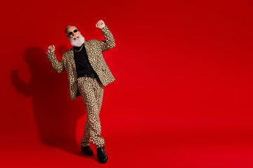 Energetic senior man wearing a stylish leopard print suit and glasses poses on a vibrant red...