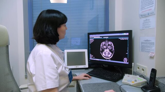 Female doctor carefully examines a brain scan displayed on a computer monitor, utilizing specialized medical software in a modern hospital or clinic setting