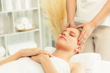 Caucasian woman enjoying relaxing anti-stress head massage and pampering facial beauty skin recreation leisure in dayspa modern light ambient at luxury resort or hotel spa salon. Quiescent
