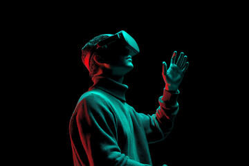 Person wearing VR headset, hand outstretched, illuminated by red and teal light against black background, showcasing virtual reality experience and technological advancement
