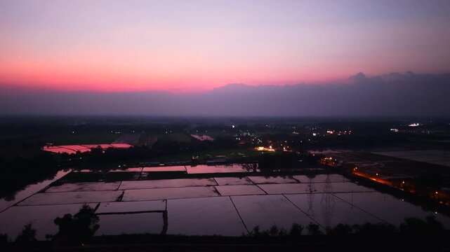 Sunlight reflects off the crop waters of the Nakhon Sawan Plain near the road at dusk
