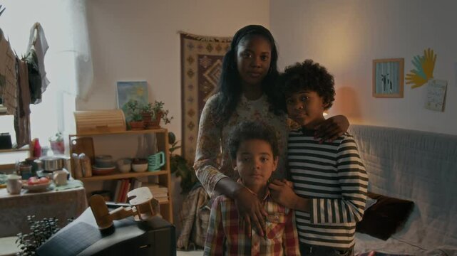 Group portrait shot of poor African American family of mother and two boys looking at camera in small lived-in apartment
