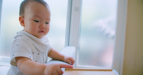 Curious Asian Baby Exploring Home Environment on Sofa in Bright Living Room with Natural Light with a curious expression.