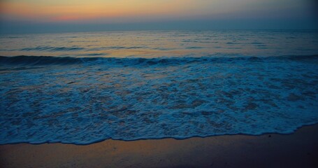 Obraz premium Tranquil ocean scene at sunset with gentle waves Gently Lapping Against a Sandy Beach Horizon and a colorful sky, perfect for relaxation and nature themes.
