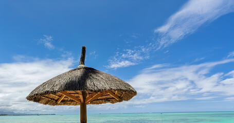 Traditional Thatched Beach Umbrella Against Turquoise Ocean and Blue Sky.Authentic Beach Shade: Thatched Umbrella and Pristine Turquoise Waters