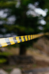 A close-up of a yellow and black caution tape stretched across an outdoor scene, symbolizing danger, restriction, and security
