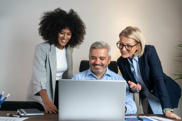 Three busy happy middle aged professional business man and two women executive leaders team using laptop working on computer at work desk having conversation on financial project at meeting in office.