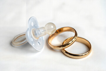 Baby Pacifier Next to Wedding Rings on Soft Background  