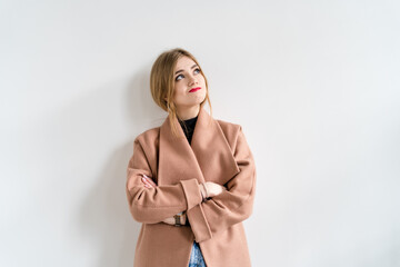 Portrait of a stylish woman standing in front of a white wall with her arms folded looking up