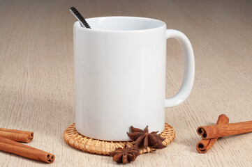 Blank 11oz white mug on the coaster on the table. Mug with spoon, cinnamon, star anise