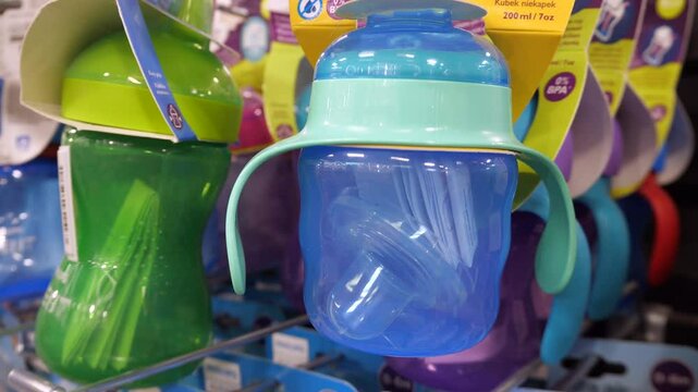 Plastic blue sippy cup and other baby sippy cups hanging on a shelf in a store. Close-up of new baby sippy cups.