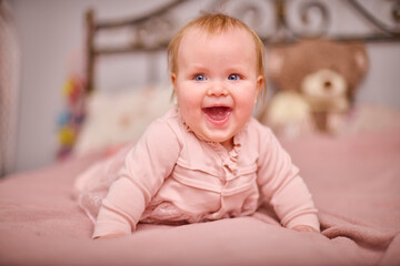 Fototapeta premium Young female with blonde hair, light skin, smiles joyfully while lying on pink bed. Soft lighting and ornate headboard create cozy, warm atmosphere