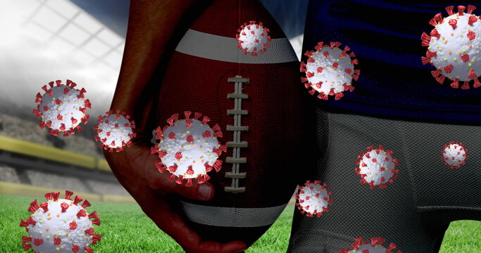 Covid-19 cells floating against mid section of male rugby player holding ball against sports stadium - Powered by Adobe