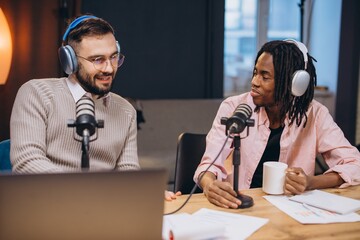Two young men are recording a podcast using professional microphones and headphones, sitting at a...