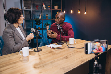 Two diverse podcasters are recording a podcast in a professional studio, engaging in a conversation