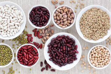 Variety of beans in bowls on textile background from above top view, closeup, copy space, healthy food and diet concept