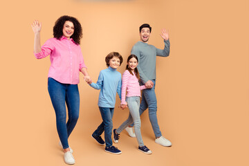 Fototapeta premium Happy family of four wearing casual outfits waving and smiling on a beige background, symbolizing joyful bonding and love