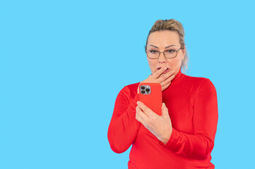 Surprised woman in red top looking at smartphone with astonishment against a bright blue backdrop