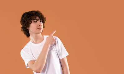 Young person with curly hair points to the side against a warm orange background, expressing...