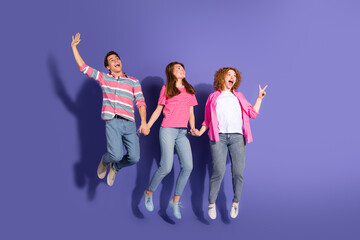 Fototapeta premium Three smiling friends jumping together on a vibrant purple background, showcasing cheerful emotions