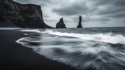 Black sand beach with surreal basalt columns rising like geometric towers waves crashing dramatically