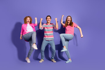 Fototapeta premium Excited group of three young friends celebrating happiness and positivity in casual fashion against a vibrant purple background