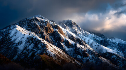 Golden light touches the snowy mountain tops under a fading sky.