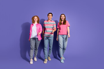 Fototapeta premium Three young friends walking together against a purple backdrop, showcasing casual fashion and cheerful expressions