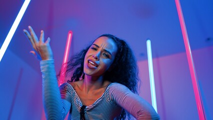 Low angle camera of hispanic dancer looking at camera and dancing to city pop music. Professional attractive hipster moving to hip hop song with purple led or neon light. Stylish cloth. Regalement.