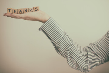 Close-up of a woman's outstretched Hand holding wooden building blocks spelling the word Thanks