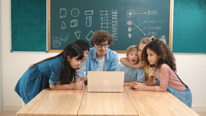 Caucasian teacher and diverse student looking at laptop at classroom. Cute multicultural children...